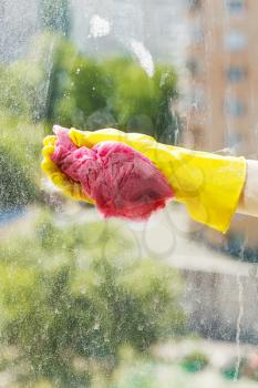 hand in yellow rubber glove washing window glass by soapy water