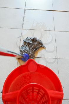cleaning the tile floor by swab and red bucket with washing water