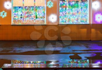 christmas illumination on urban house wall, wet wooden bench and rain puddle in winter night