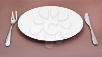 empty white porcelain plate with fork and knife on brown background