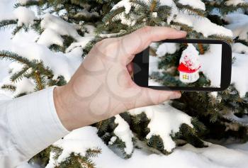 travel concept - tourist taking photo of new glass white house on Christmas tree outdoors on mobile gadget