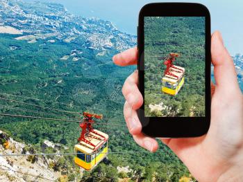 travel concept - tourist taking photo of Cableway Miskhor - Ai-Petri over Crimean mountains on mobile gadget, Crimea