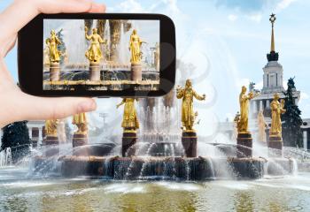 travel concept - tourist takes picture of Fountain Friendship of Nations at All-russia Exhibition Center in Moscow on smartphone,