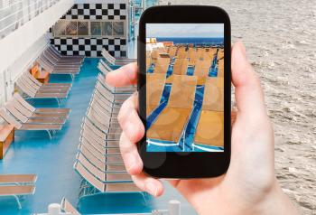 travel concept - tourist takes picture of outdoor relaxation area on stern of cruise liner on smartphone,