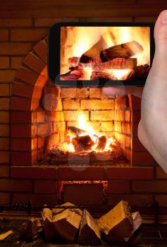 travel concept - tourist takes picture of burning wood in fireplace in evening time on smartphone,