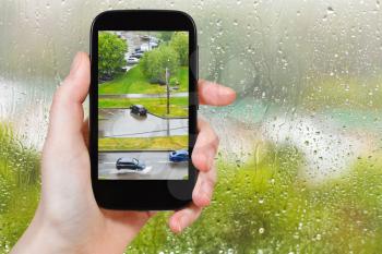 travel concept - tourist takes picture of shower in city from home window on smartphone,