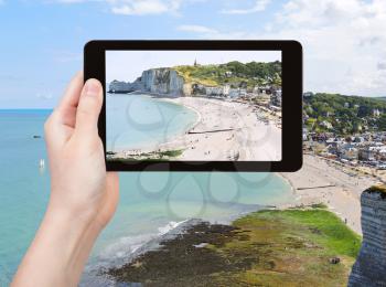 travel concept - tourist takes picture of Etretat resort village on english channel beach of cote d'albatre, France on tablet pc