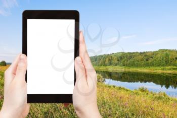 travel concept - tourist photograph green grass on riverbank in summer day, Vologda, Russia on tablet pc with cut out screen with blank place for advertising logo