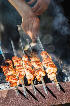 man cooks pork kebabs on outdoor grill