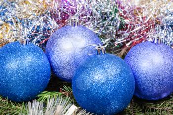 Christmas still life - four blue and violet Christmas balls, colorful tinsel on Xmas tree background