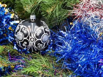 Christmas still life - one black glass Christmas ball, blue tinsel on Xmas tree background
