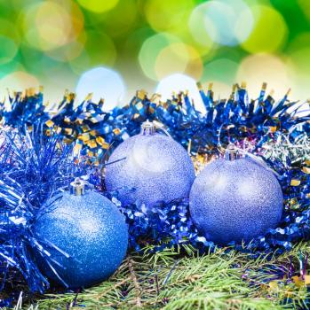 Xmas still life - blue balls, tinsel at green tree with blurred green Christmas lights background