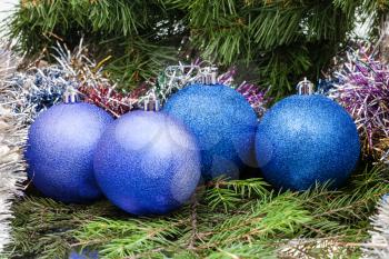 Christmas still life - four blue and violet Christmas baublels, tinsel on Xmas tree background