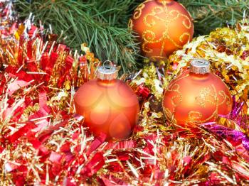 Christmas still life - three orange and yellow Christmas balls, red tinsel on green Xmas tree background