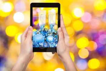 man takes photo of Christmas still life - two glasses of champagne at blue Xmas tinsel with yellow and violet blurred Christmas lights background