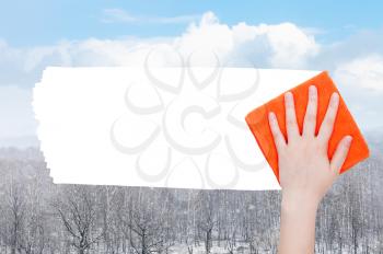 weather concept - hand deletes snow over forest by orange rag from image and white empty copy space are appearing