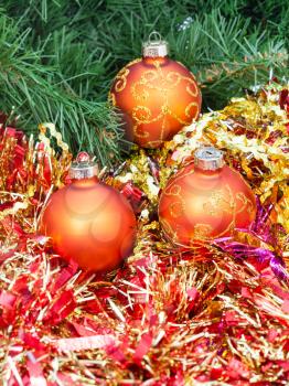 Christmas still life - three orange and yellow Christmas baubles, red tinsel on green Xmas tree background