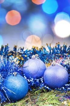 Xmas still life - blue balls, tinsel at green tree with blurred blue Christmas lights bokeh background