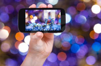 man takes photo of Christmas still life - two glasses of champagne at blue Xmas decorations with dark violet and red blurred Christmas lights bokeh background