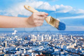 nature concept - hand with paintbrush paints blue sky over big city