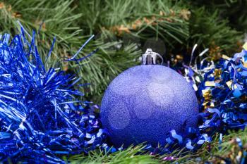 Christmas still life - one violet Christmas ball, tinsel on Xmas tree background
