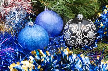 Christmas still life - one black glass and two blue and violet Christmas balls, tinsel on Xmas tree background