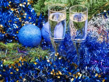 Christmas still life - Two glasses of sparkling wine with blue Xmas decorations on green Christmas tree background