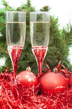 Christmas still life - Two glasses of champagne with red Xmas baubles and tinsel on Christmas tree background