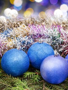 Xmas still life - blue balls, tinsel at green tree with blurred violet Christmas lights bokeh background