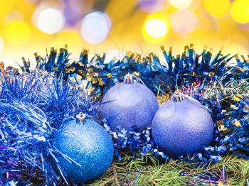 Xmas still life - blue balls, tinsel at green tree with blurred yellow Christmas lights bokeh background