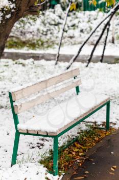 first snow on bench in city park in autumn day