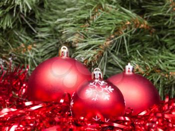 Christmas still life - three red Christmas baubles, tinsel on Xmas tree background