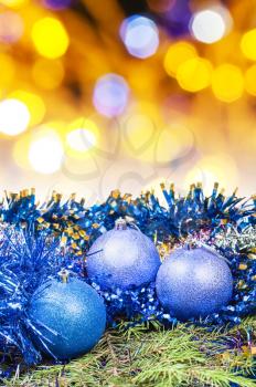 Xmas still life - blue balls, tinsel at green tree with blurred yellow and violet Christmas lights bokeh background