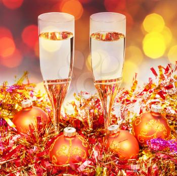 Christmas still life - two glasses of champagne at golden Xmas decorations with dark red and yellow blurred Christmas lights bokeh background