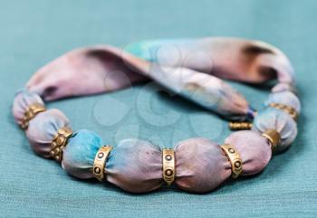 textile necklace from pink and blue painted silk and bronze beads on green background
