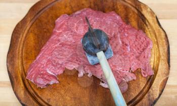 top view of slice of raw veal is beating by meat tenderizer on cutting board