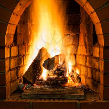 open fire in fire-box of brick fireplace in country cottage