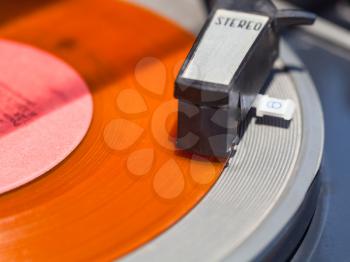 tonearm of record-player on orange vinyl disc close up