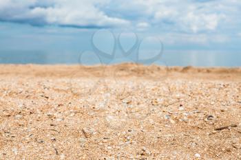 Foreground focus - sand and shelly beach close up and white clouds over blue sea. Coasline of Sea of Azov, Temryuk bay, Golubitskaya resort, Taman peninsula, Kuban, Russia