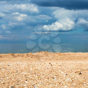 Foreground focus - sand and shelly beach close up and dark blue clouds over sea. Coastline of Sea of Azov, Temryuk bay, Golubitskaya resort, Taman peninsula, Kuban, Russia
