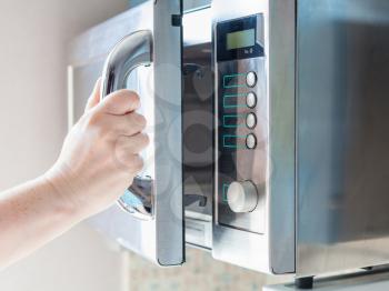 hand opens door of microwave oven for cooking food
