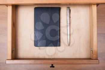 above view of silver pen and black notebook in open drawer of nightstand