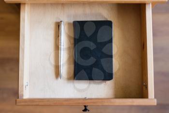 top view of vintage pen and black notebook in open drawer of nightstand