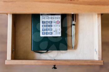 top view of pen, calculator and notebook in open drawer of nightstand
