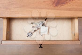 top view of bunch of door keys with keychain in open drawer of nightstand