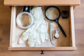 above view of magnifying glasses, tweezers and white gloves in open drawer of nightstand
