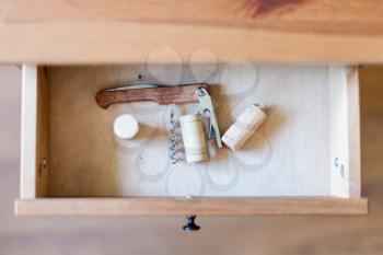 above view of foldable corkscrew and few corks in open drawer of nightstand