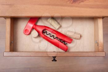 above view of red corkscrew and cork from wine bottles in open drawer of nightstand