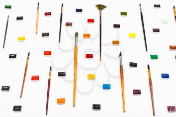 side view of many paint brushes and watercolors arranged on white background