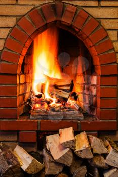 pile of firewood and firewood burning in indoor brick fireplace in country cottage